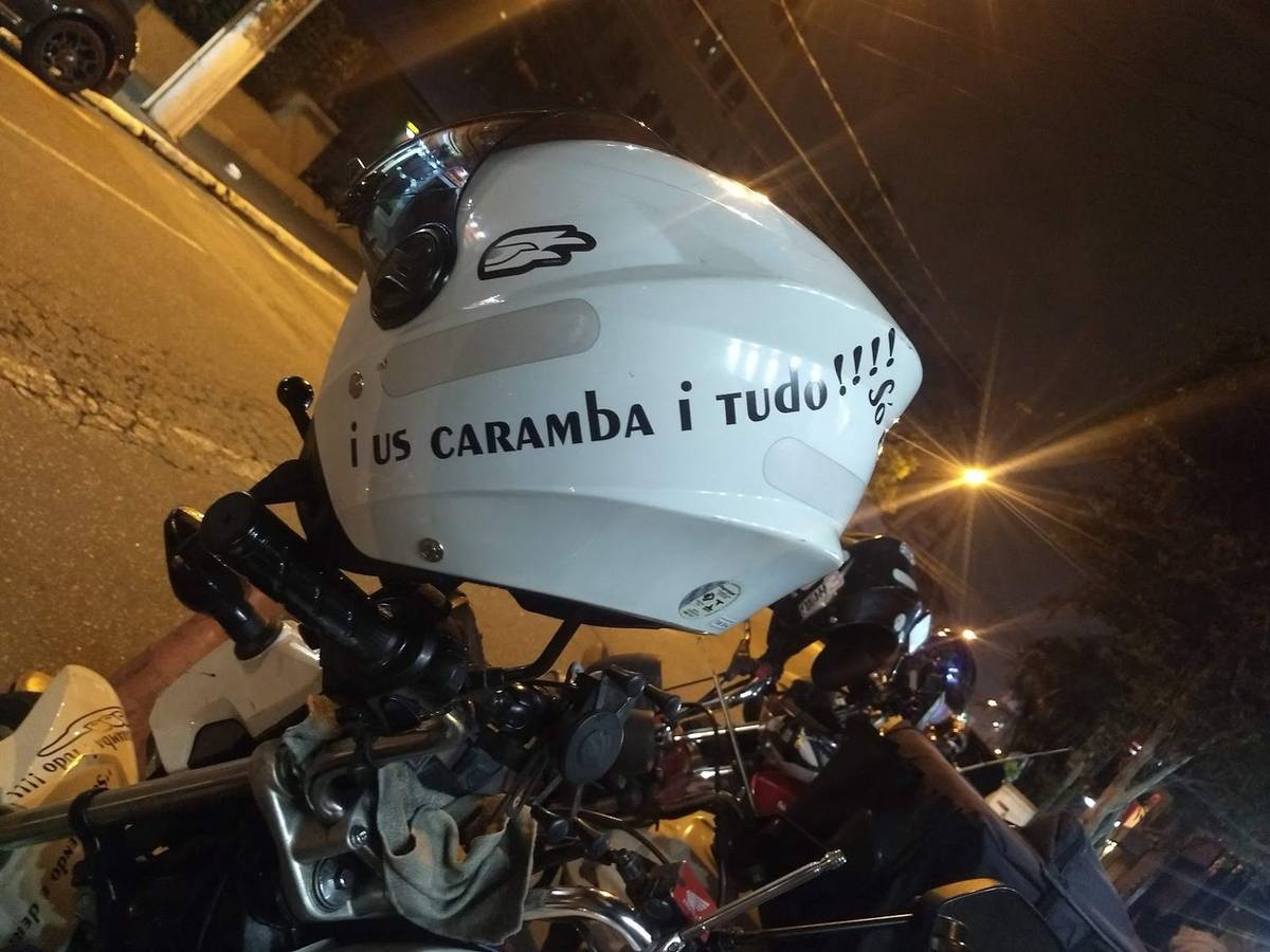 Capacete branco apoiado no guidão de uma moto, fotografado de perto na rua à noite.